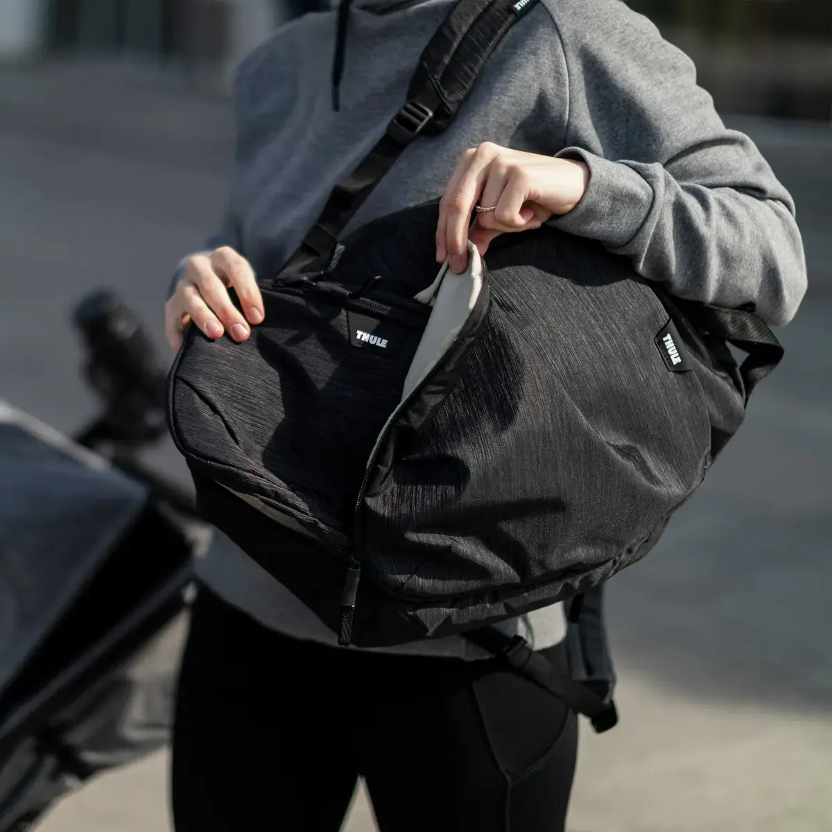 Parent opening the Thule Changing Backpack whilst out with a pushchair