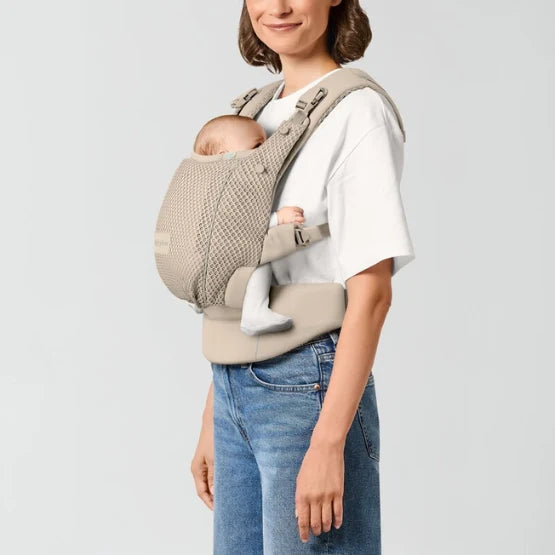 Woman wearing a beige mesh soft structured baby carrier with newborn in front inward carry position