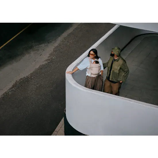 Aerial view of two parents with baby carried in the Cybex Amya Baby Carrier in Sandy Beige, urban outdoor setting