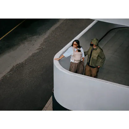 Aerial view of two parents with baby carried in the Cybex Amya Baby Carrier in Sandy Beige, urban outdoor setting