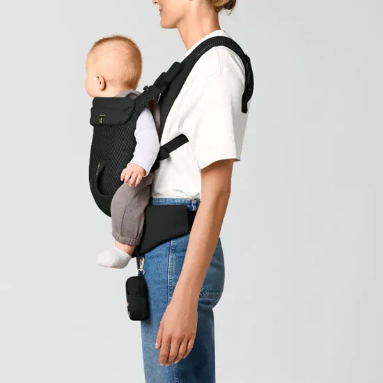 Parent carrying older baby in back carry position in the Cybex Laya Baby Carrier in Black, side view with storage pouch clipped to hip