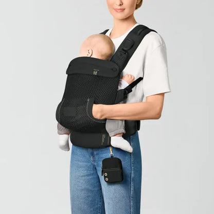 Parent carrying baby in inward-facing front position in the Cybex Laya Baby Carrier in Black, side view with storage pouch visible