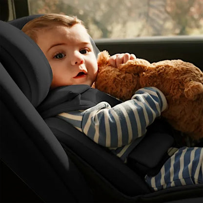 Baby cuddling a teddy, harnessed and comfortable in the Silver Cross Motion 3 i-Size car seat by the car window