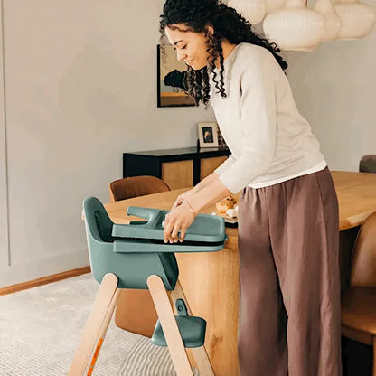 Parent fitting the tray to the UPPAbaby Ciro V2 High Chair in Betsy spruce green beside a dining table