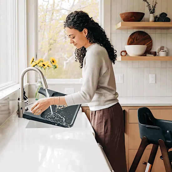 Parent rinsing the UPPAbaby Ciro V2 tray liner under the kitchen tap